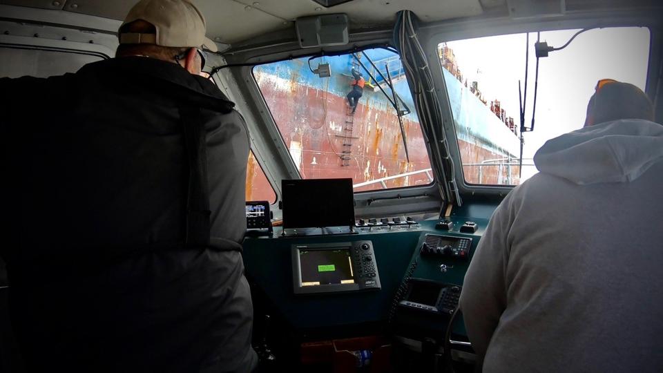 Crew members watch a bar pilot ascend a rope ladder.