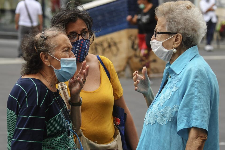 Elderly women wearing surgical face masks, talking on the street.