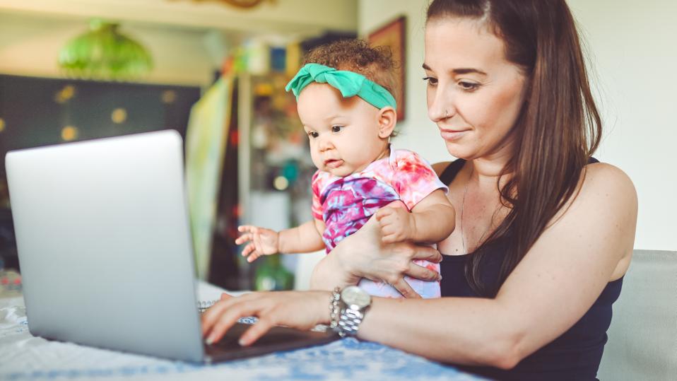 Mother and baby sit in front of a laptop at home, working, video chat or telemedicine