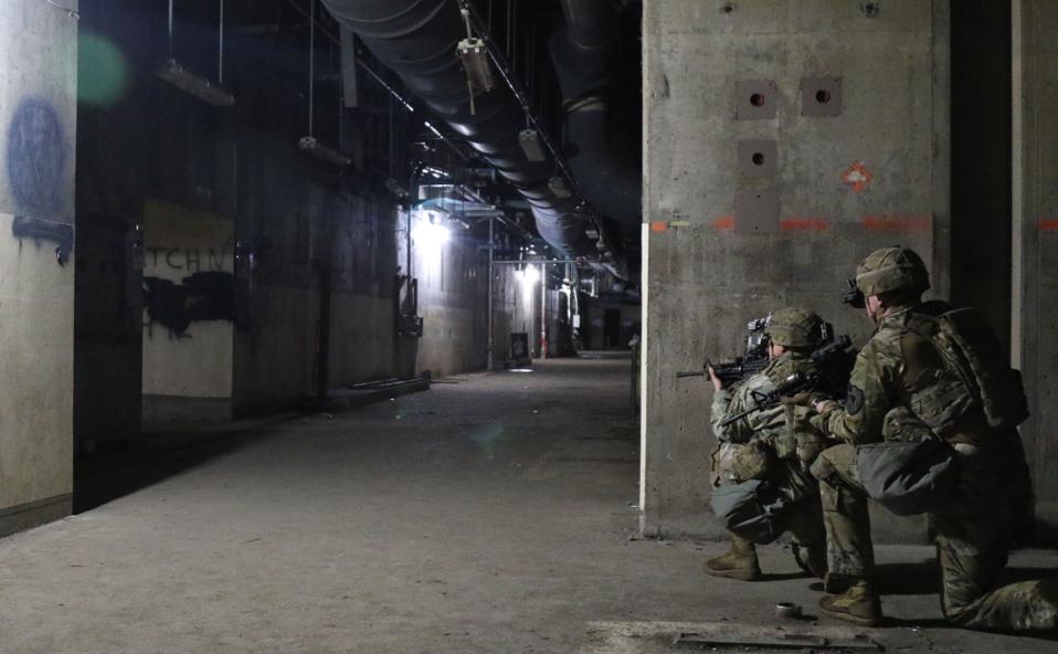 Two soldiers hold rifles at the ready in an underground corridor.