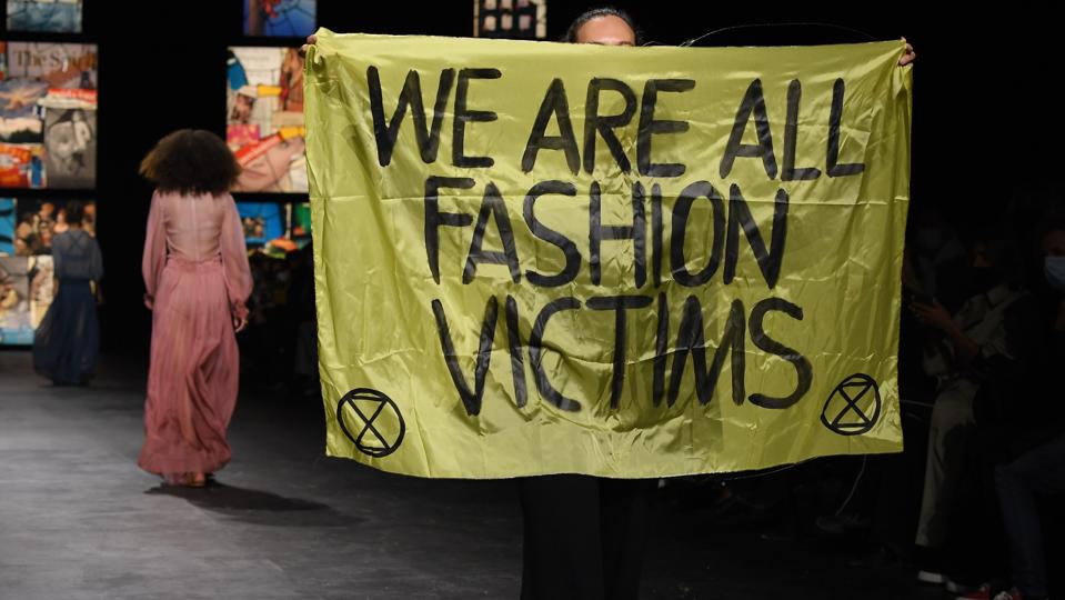 Extinction Rebellion protestor on Dior runway with flag reading We are all fashion victims