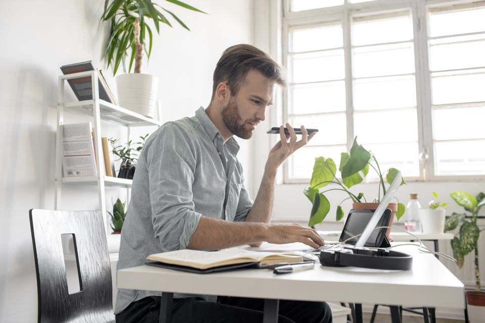 Man using smartphone and laptop at desk in office