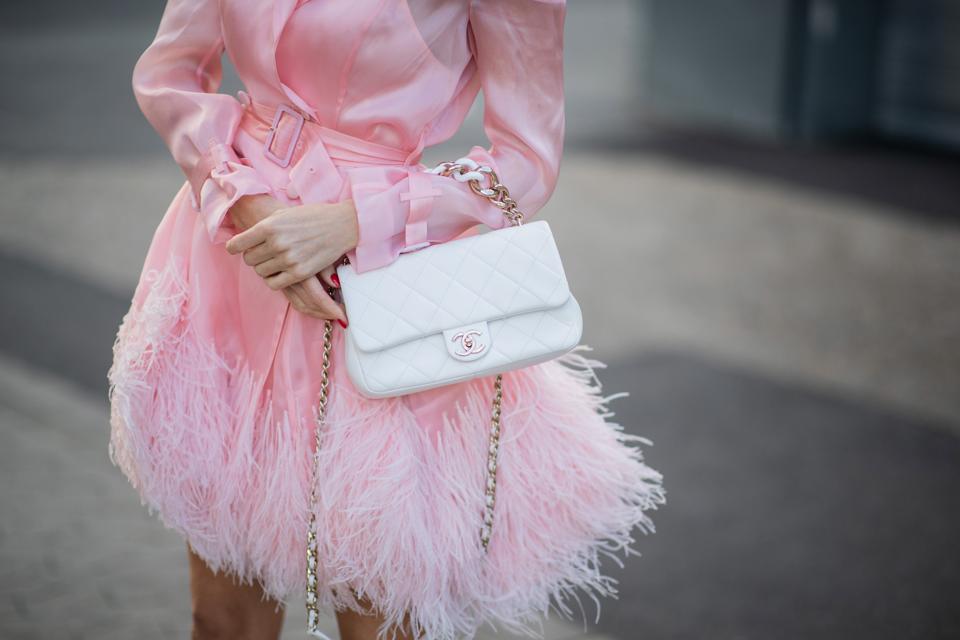 Body shot of woman wearing a pink dress holding a white Chanel handbag