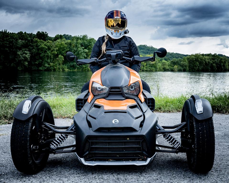 A woman sits atop a Can-Am Ryker, a three-wheeled motorbike.