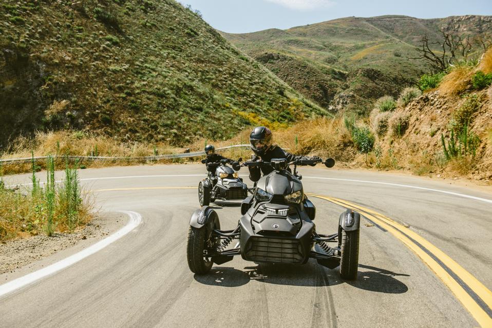 Two black trikes whip around a tight bend at speed in the California hills.