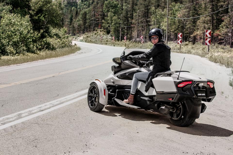 A woman rides a Can-Am Spyder on the side of a highway.