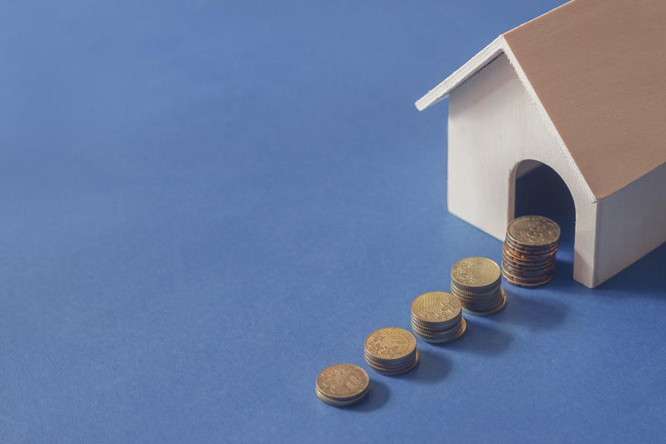 Buying new house concept. Gold coin and toy house on blue background