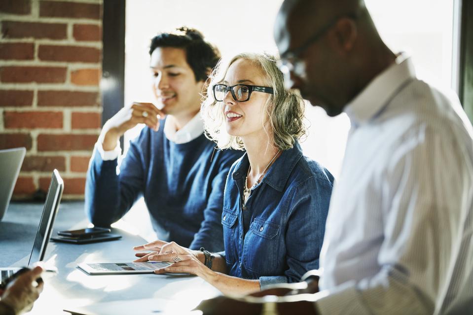 Smiling businesswoman leading meeting with clients and colleagues in coworking space