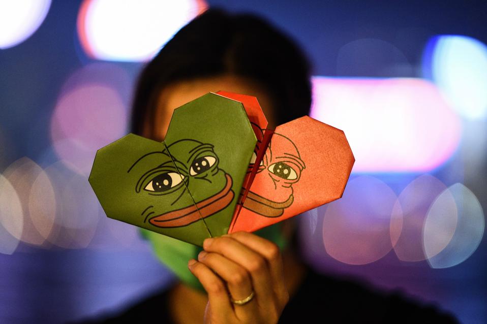 A woman holding origami hearts with a depiction of Pepe the Frog, a meme character.