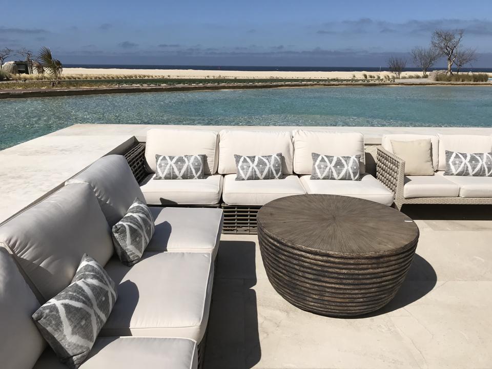 Gray couches next to a large pool, with a beach and ocean in the background