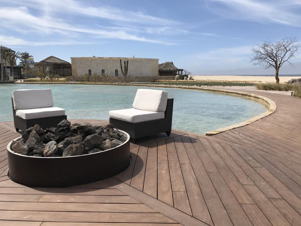 Two chairs next to a fire pit, in front of a pool; in the background is the spa and the beach.