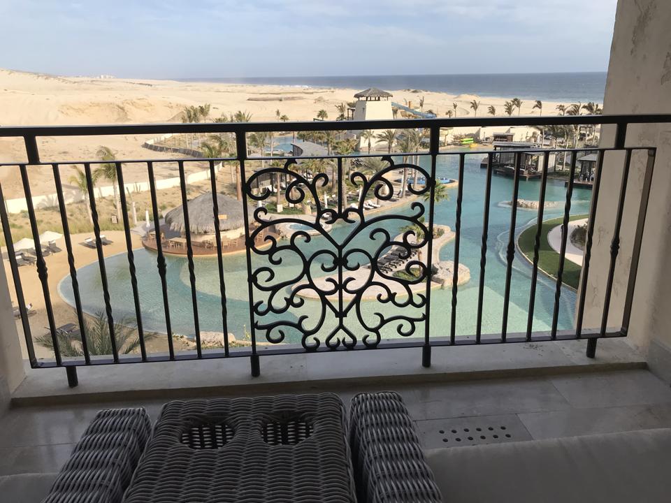 Through the iron railings of the balcony, the twisting blue of the lagoon pool with its palm tress and poolside restaurants, with empty sand dunes and the ocean in the background
