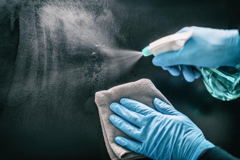 Surface home cleaning spraying antibacterial sanitizing spray bottle disinfecting against COVID-19 spreading wearing medical blue gloves. Sanitize surfaces prevention in hospitals and public spaces