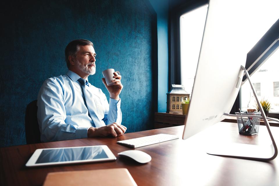 Focused mature businessman deep in thought while sitting at a table in modern office.