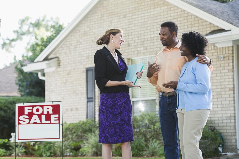 Agent talking with couple in front of house for sale