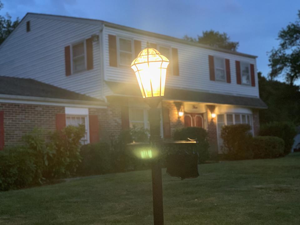 Front yard lamppost shining brightly at dusk in front of a cozy home