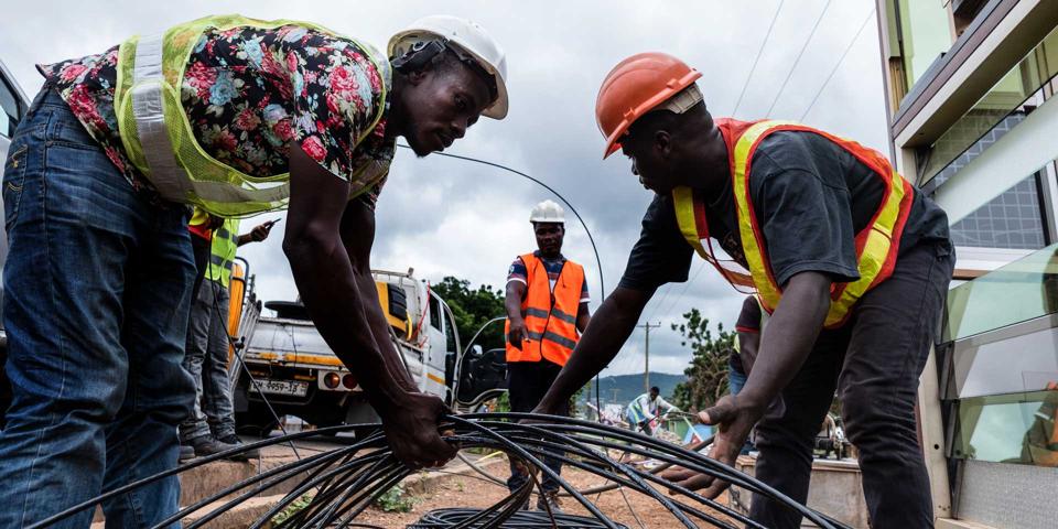 African men in hard hats lay down fiber wire under the supervision of a manager