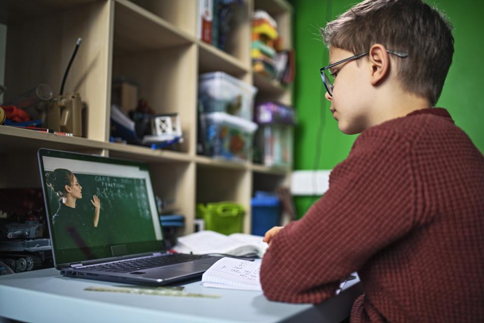 Little boy during COVID-19 quarantine attending to online school class from his room.