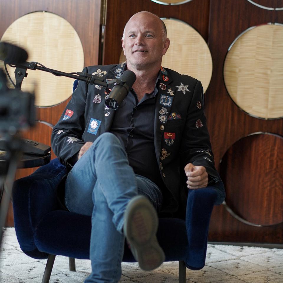 Mike Novogratz sitting in low chair with microphone in front of face during interview
