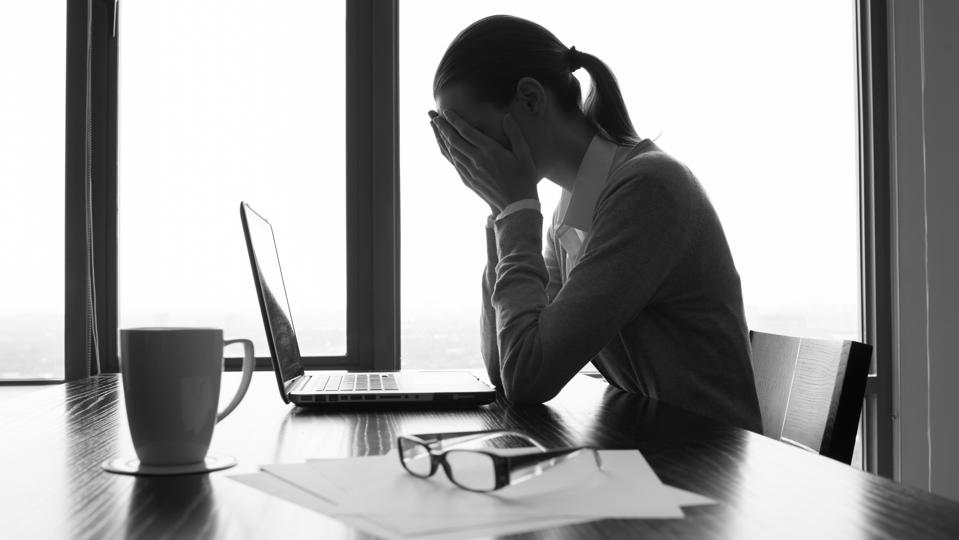 a female office worker with her hands in her face, stressed and dejected