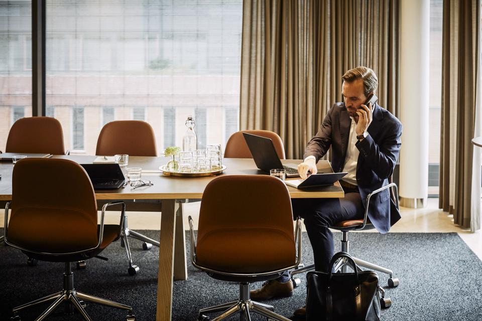 Full length of legal professional talking on mobile phone while writing in diary at board room