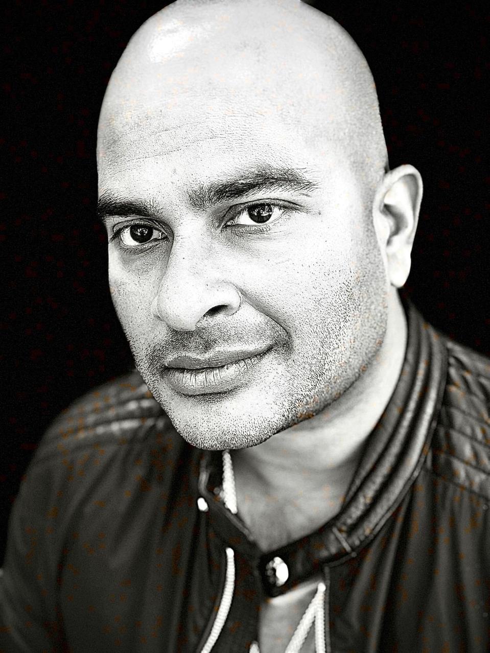 A black and white headshot of a bald man in a dark jacket