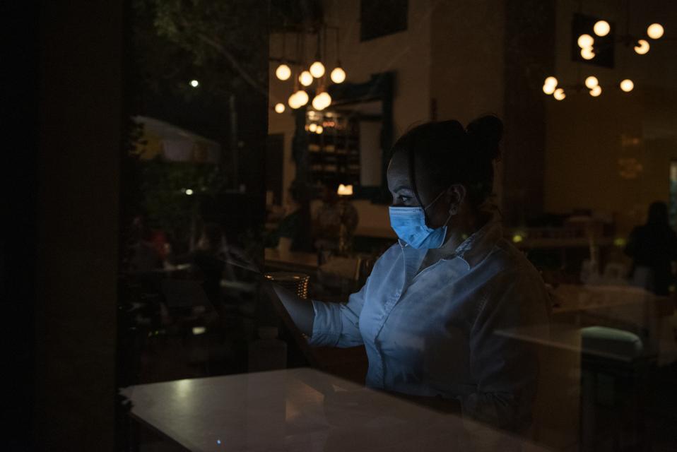 Waitress wearing a face mask standing in a dark restaurant