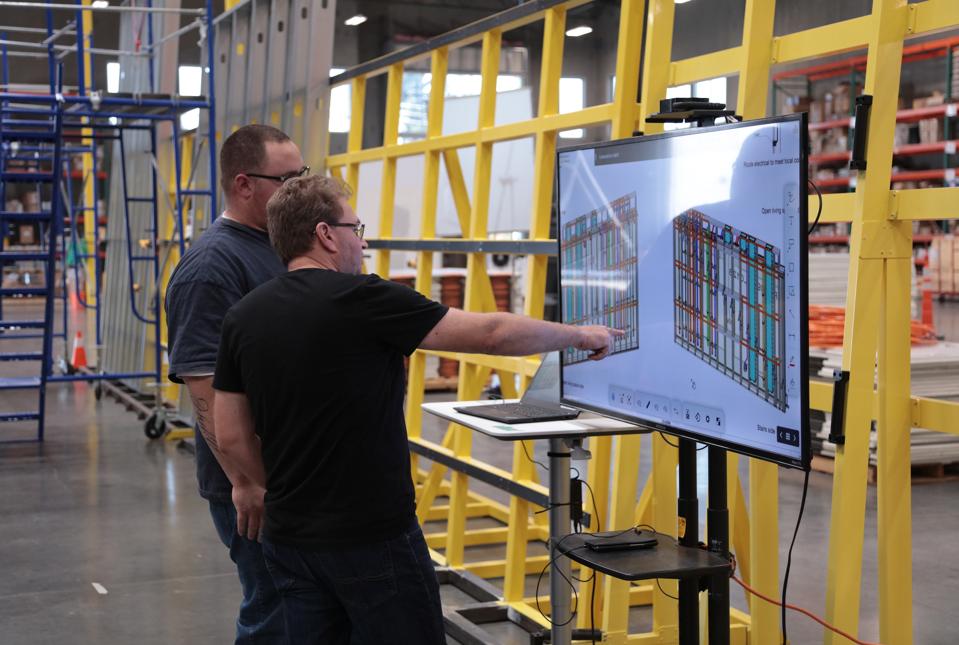 Amit Haller, CEO and co-founder of Veev (front), talks to a team member about building designs, in his factory where walls are being assembled in the background.