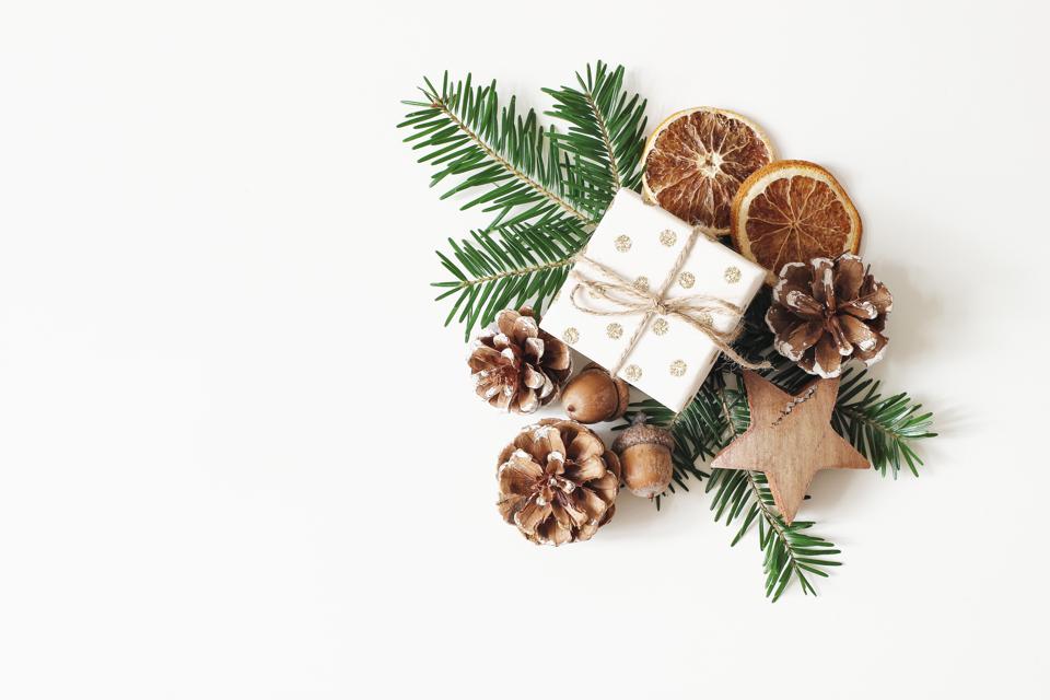Christmas festive styled stock composition. Hand wrapped gift box, dry orange fruit slices, acorns, pine cones and fir tree branches isolated on white table background. Winter flat lay, top view.