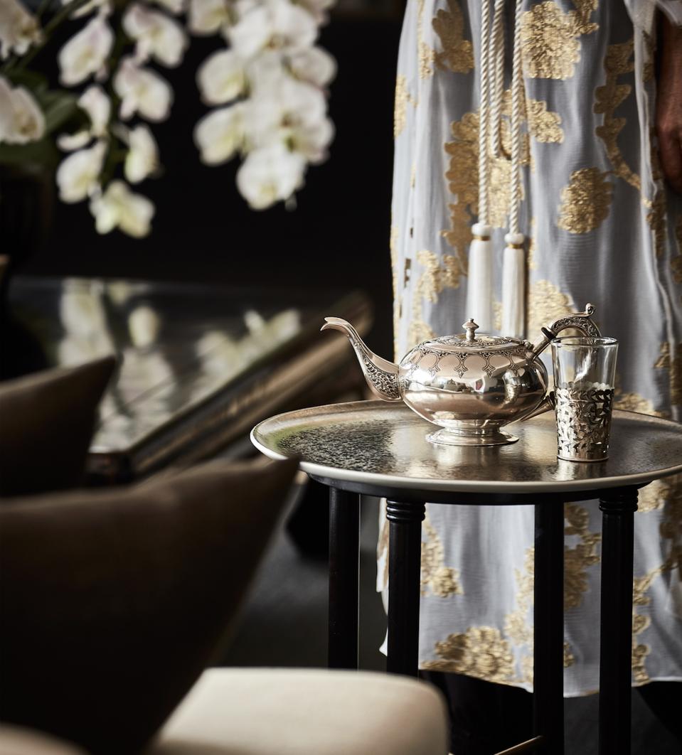 A Moroccan teapot on a table and a woman wearing a lovely Marie France Van Damme caftan.