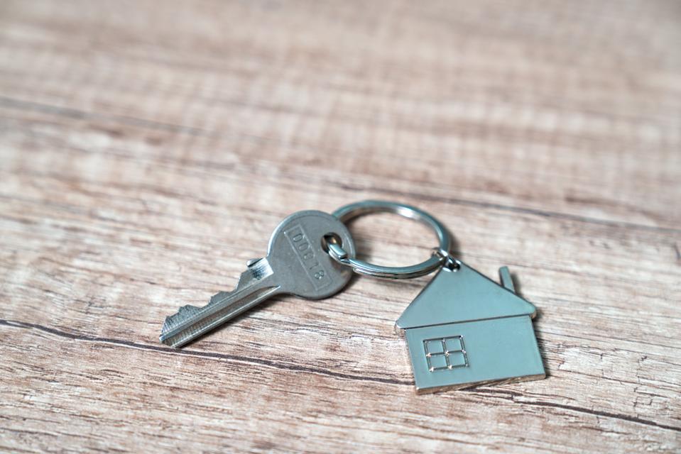House key on a house shaped keychain resting on wooden floorboards concept for real estate, moving home or renting property