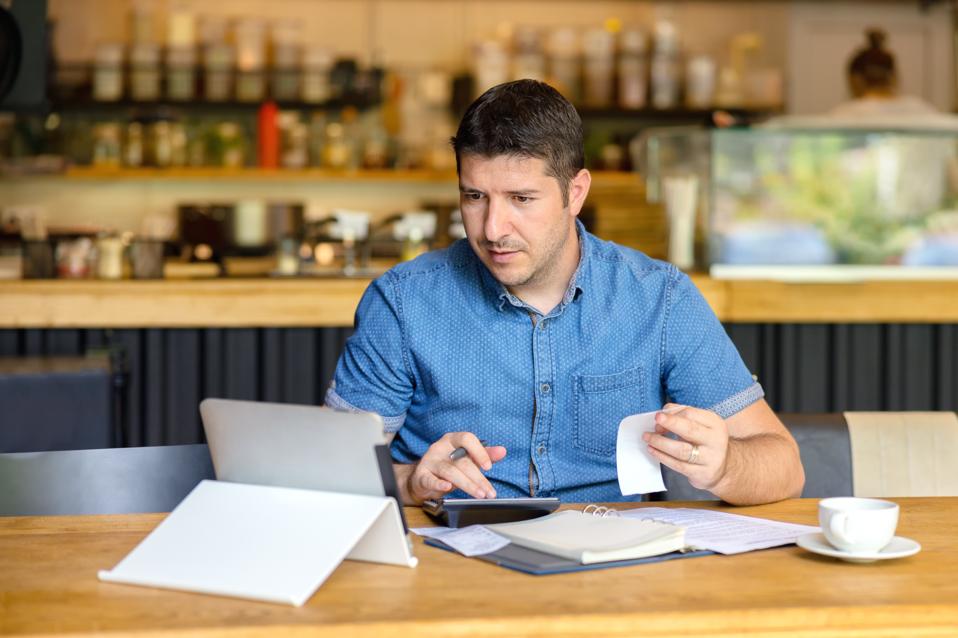 Mature small business owner calculating finance bills of activity - Entrepreneur using laptop and calculator to work and to calculate and analyze financial expenses of new business start-up