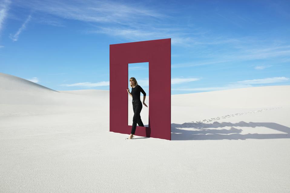 Young fashion model walking through red door frame at desert against sky