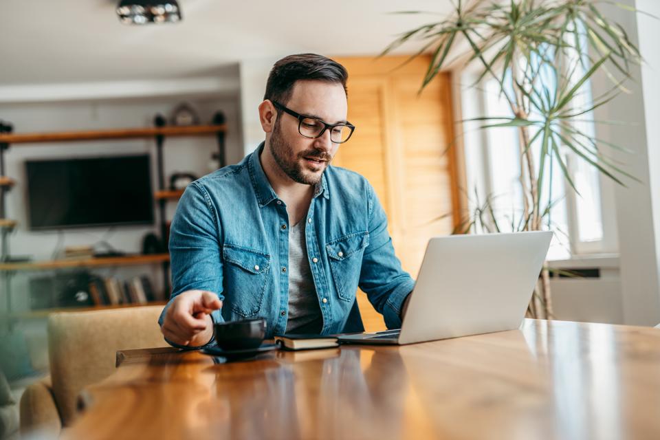 Portrait of a handsome man having video call on laptop and drinking cup of coffee.