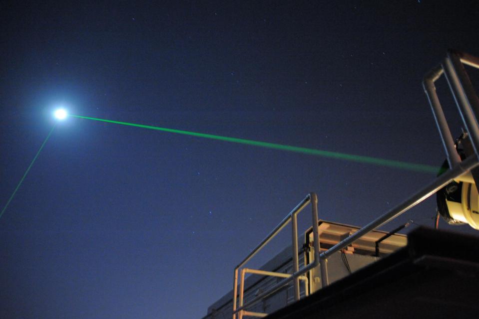 Color photo of a green laser beam shooting into the night sky.