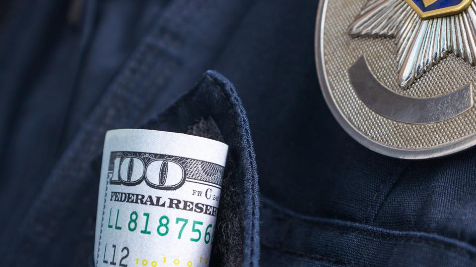100 US dollar bill in a pocket of a police officer uniform. Symbolic image of bribe, police corruption. Close-up, selective focus.