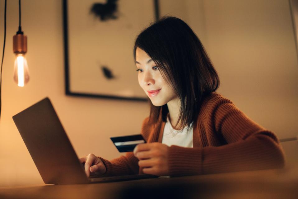 Mujer joven comprando en línea con computadora portátil y tarjeta de crédito en casa