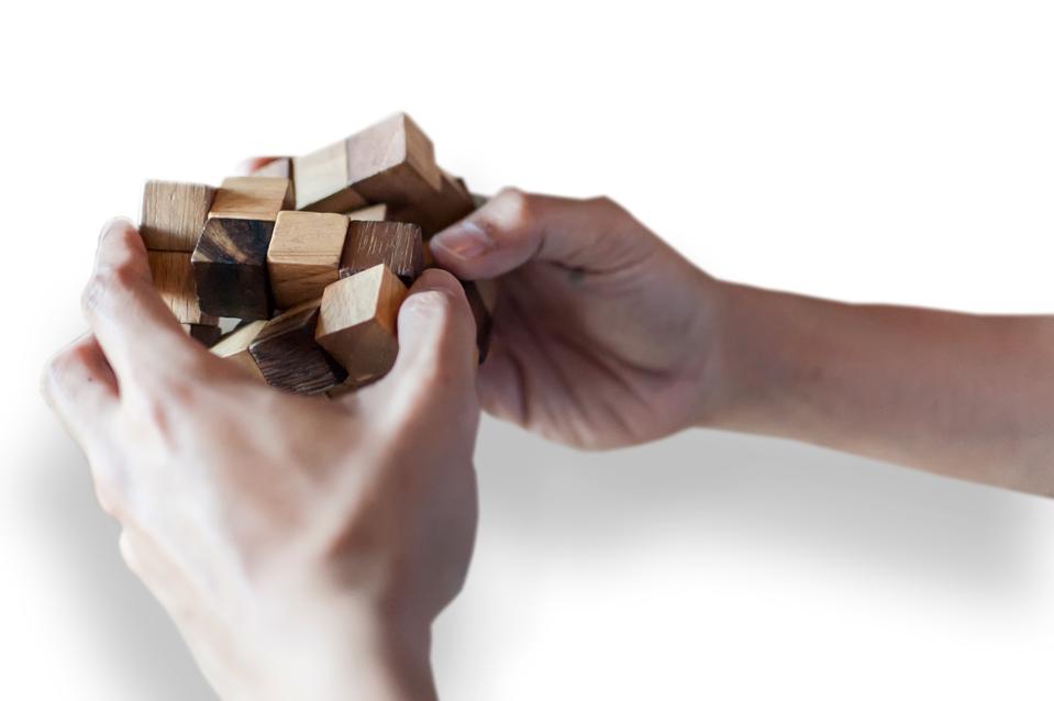 Close-Up Of Hand Holding Puzzle Cube Over White Background