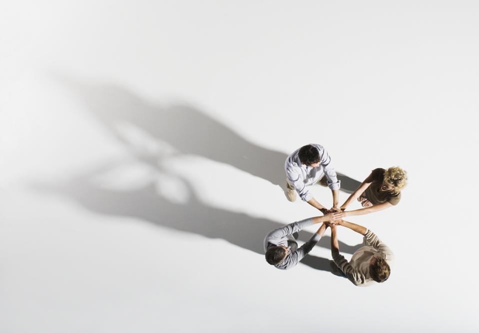 Four people placing hands over each other's, overhead view