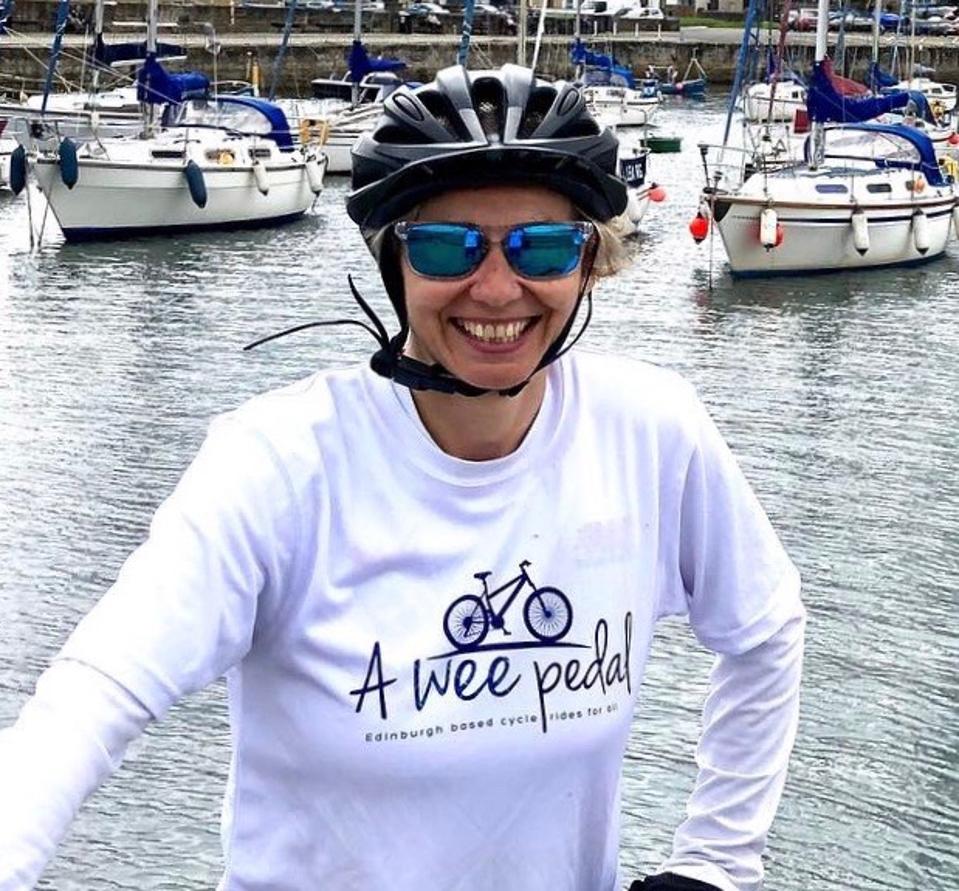Leanne smiles wearing cycle helmet by a river