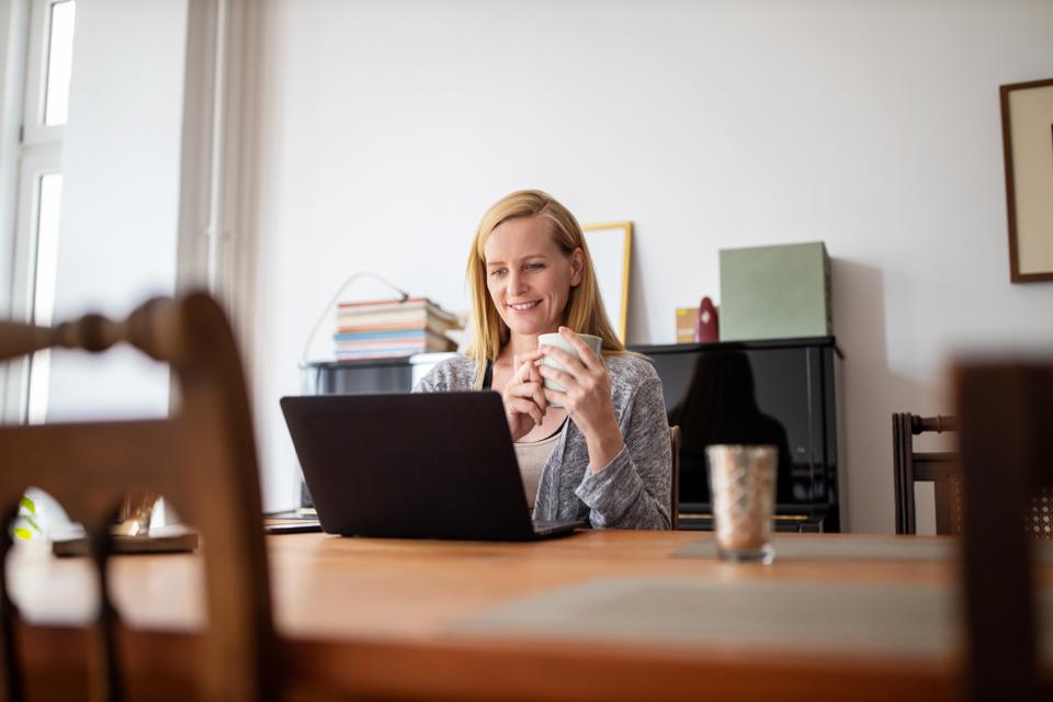 Woman having coffee and using laptop at home