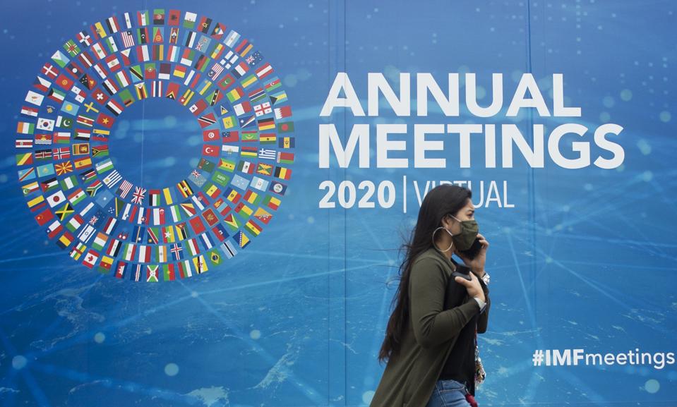 A woman walks past a promotional poster for the virtual 2020 Annual Meetings outside the International Monetary Fund at their headquarters in Washington, DC on October 13, 2020.