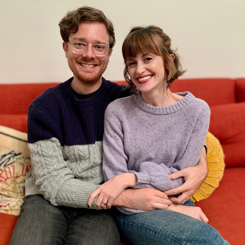 A couple sits on an orange sofa.