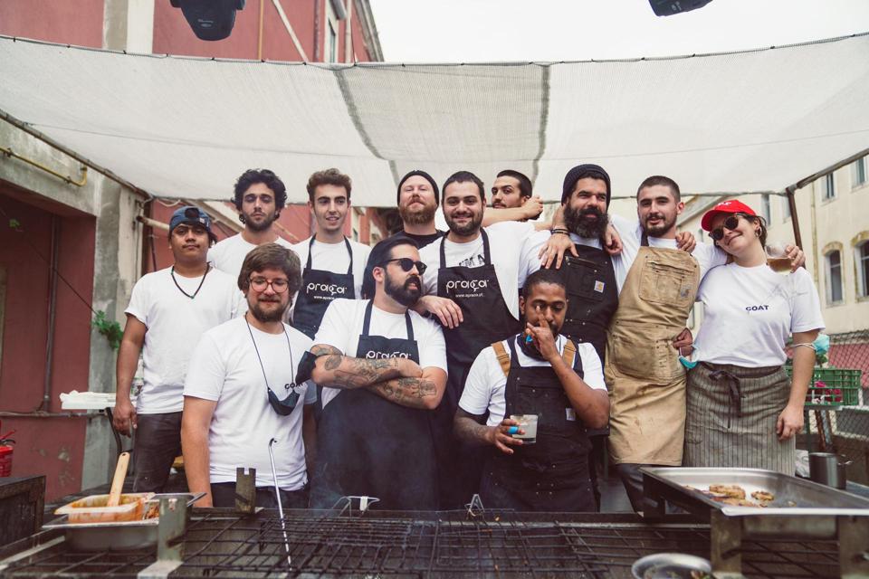 A group of chefs in Portugal stands in front of a grill during an outdoor meal in Lisbon