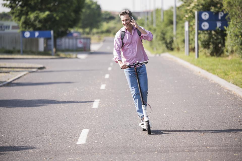 Businessman using smartphone riding his E-Scooter