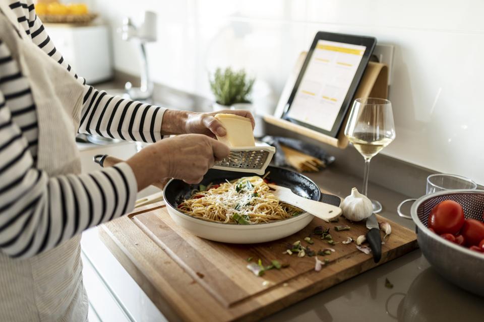 Primer plano de mujer con tableta cocina plato de pasta en la cocina de casa