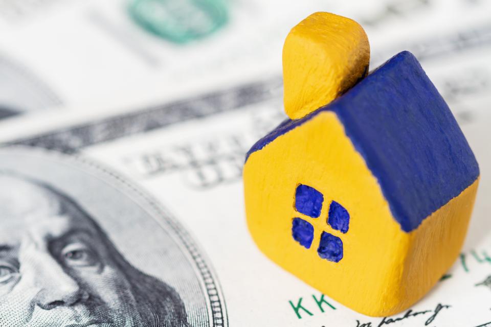 Miniature yellow toy house with a blue roof on 100 (one hundred) dollars bill. Selective focus.