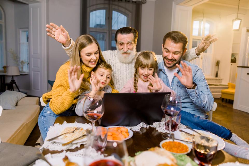 Beautiful family, sitting at the table with dinner meal, smiling, happy and using laptop. Family making videocall using laptop celebrating at home