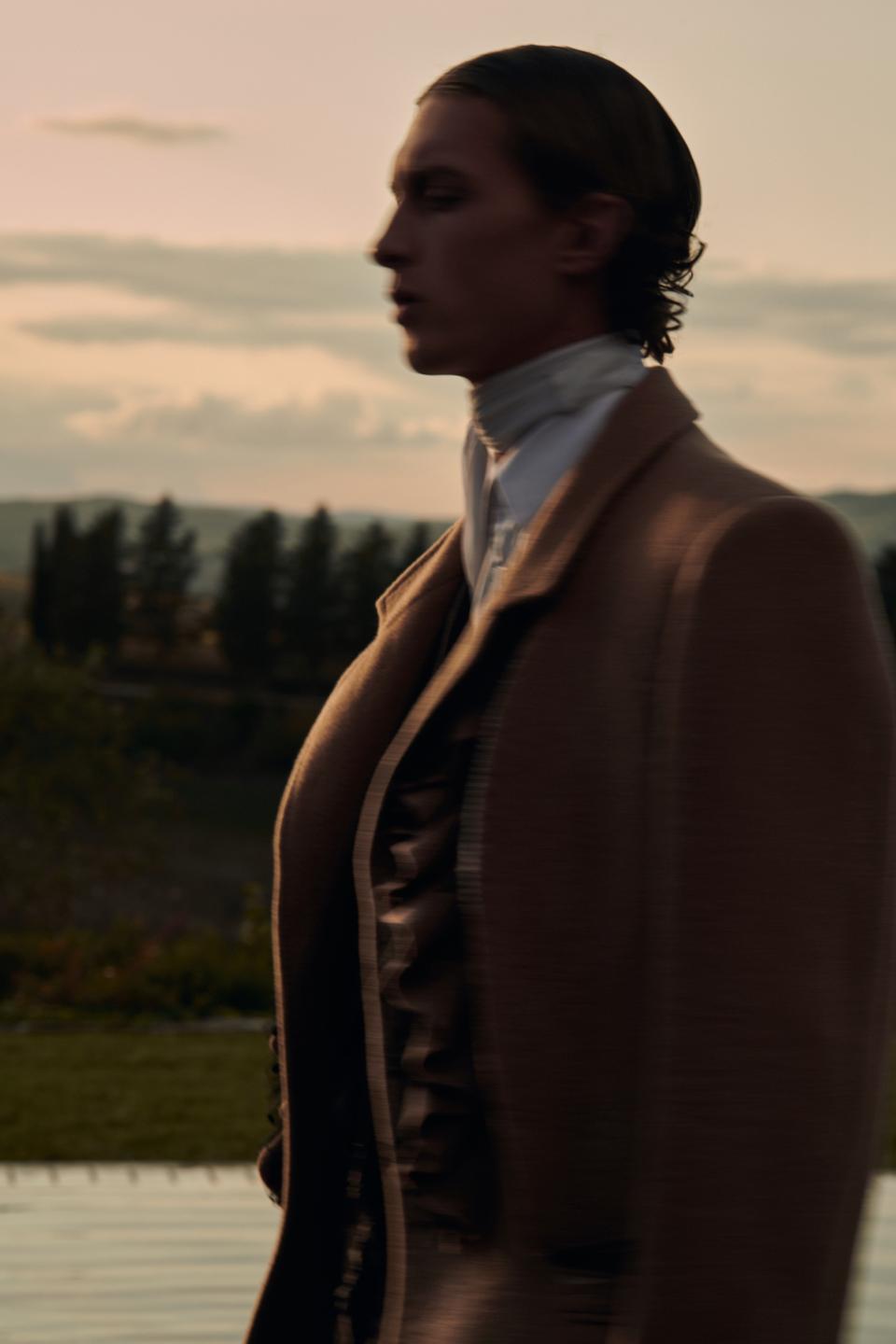 Camel wool overcoat with frill cuts revealing the lining, worn over a burgundy and black pinstripe wool mohair suit with inserted frills and a white shirt.