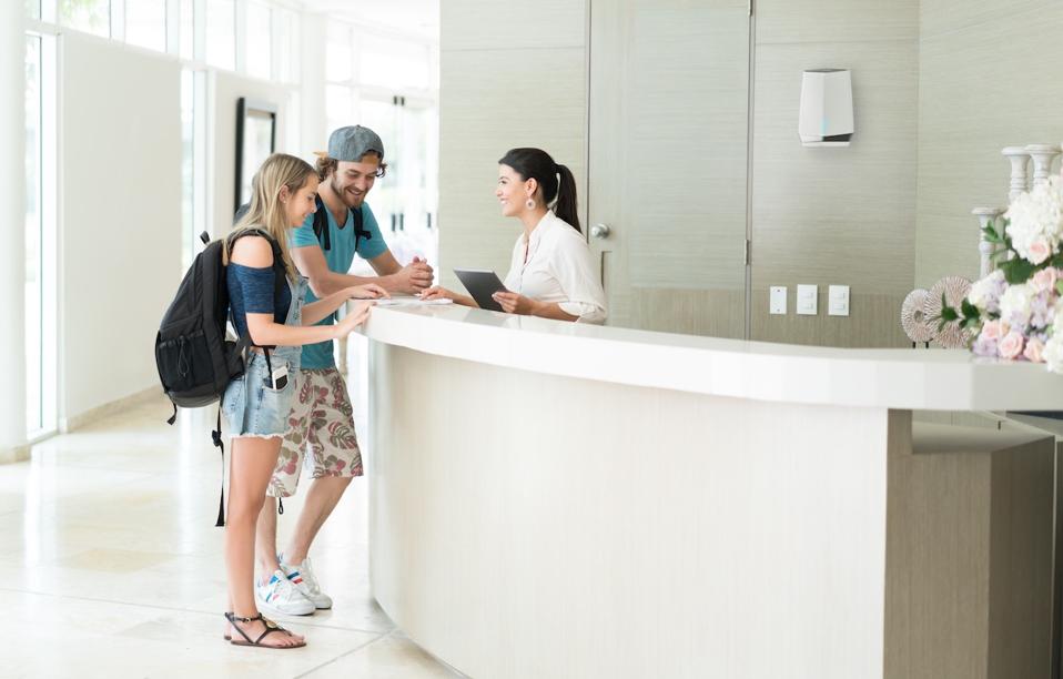 Two people checking into a hotel with a Netgear Orbi Pro behind the desk.